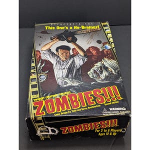 May include: A board game box titled "ZOMBIES!!!" features a man holding a chainsaw above his head, with zombie figures in the background. The box has the text "Director's Cut" and "This One's a No-Brainer!" printed on it. The game is for 2 to 6 players, ages 12 and up.