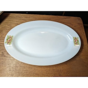 May include: White oval serving platter with floral accents. The platter has a smooth, glossy surface and features a delicate floral design in shades of pink, yellow, and green on each end. A classic piece for serving food.