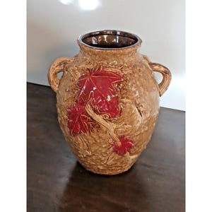 May include: A textured, brown ceramic vase with two handles and a dark brown interior. The vase features a raised relief design of red leaves and branches. The vase is a decorative home decor item.