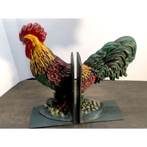 May include: A pair of cast iron rooster bookends. The rooster figures are painted in vibrant colors, including red, yellow, and green. Each bookend has a rectangular base and a vertical support to hold books upright. The bookends are designed to add a touch of rustic charm to any bookshelf.