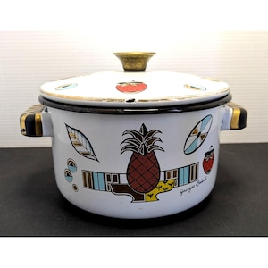 May include: White enamel pot with lid, featuring a pineapple and strawberry design. The pot has gold accents on the handles and lid, with a black rim. The lid has a gold knob and is decorated with fruit.