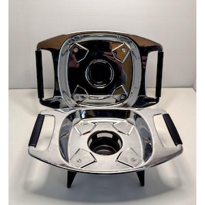 May include: Two-piece stainless steel chafing dish set. The top piece has a handle on each side and a central opening. The bottom piece has a stand with three legs and a central opening. The set is designed to keep food warm.