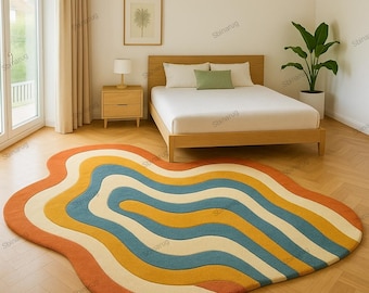 May include: A colorful, wavy area rug with a retro design. The rug features bands of orange, yellow, blue, and cream colors. The rug is placed on a hardwood floor in a bedroom setting, with a bed and nightstand visible.