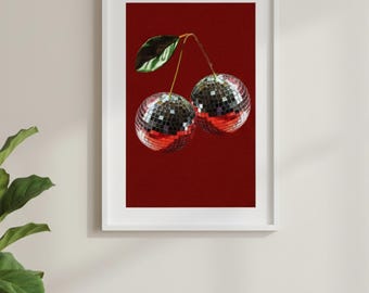 Peut inclure: Une impression encadrée représentant deux cerises avec des surfaces en boule à facettes, une feuille verte et un fond rouge. L'œuvre est présentée dans un cadre blanc, ajoutant une touche moderne à la décoration murale. L'image est posée contre un mur neutre avec une plante et un canapé gris.