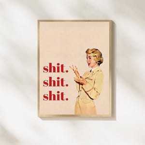 May include: A framed print with a retro illustration of a woman in a beige suit, gesturing with her hands. The word "shit" is repeated three times in red text on the left. The print has a light beige background and a wooden frame.