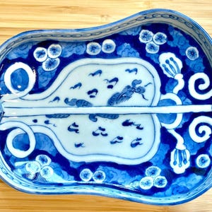 Puede incluir: Una fuente de cerámica azul y blanca con una forma única de calabaza. La fuente presenta intrincados diseños florales y de pájaros en tonos azules. El borde tiene un borde festoneado y la fuente mide aproximadamente 25 cm de largo.