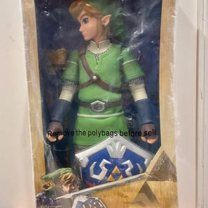 Puede incluir: Figura de acción de Link de edición limitada de la serie World of Nintendo. La figura viste una túnica y un gorro verdes, con un escudo azul. El embalaje incluye el texto "Remove the polybags before sell."