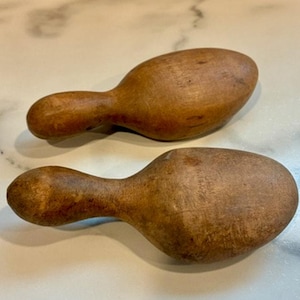 Puede incluir: Dos hormas de zapato de madera vintage con un talón redondeado y una sección de puntera ancha y cónica. Estas formas de madera natural marrón presentan un patrón de grano distintivo y una textura ligeramente desgastada y clásica.