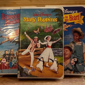 May include: Three vintage Disney VHS tapes. Titles include "Bedknob and Broomstick", "Mary Poppins", and "Disney's to my Heart". The "Mary Poppins" tape features a colorful illustration of the characters. The tapes are in good condition.