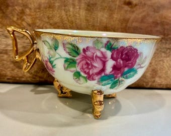 Taza de té japonesa MCM de cerámica brillante con diseño floral rosa y oro, tres patas y asa de ala de mariposa.