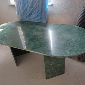 May include: A green marble oval table with a polished surface. The table has a two-leg base. The table is approximately 60 inches long and 30 inches wide.