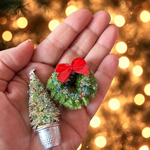 May include: Miniature Christmas tree in a silver pot and a small wreath with a red bow. The tree is green with colourful beads and a silver star. The wreath is green with colourful beads.