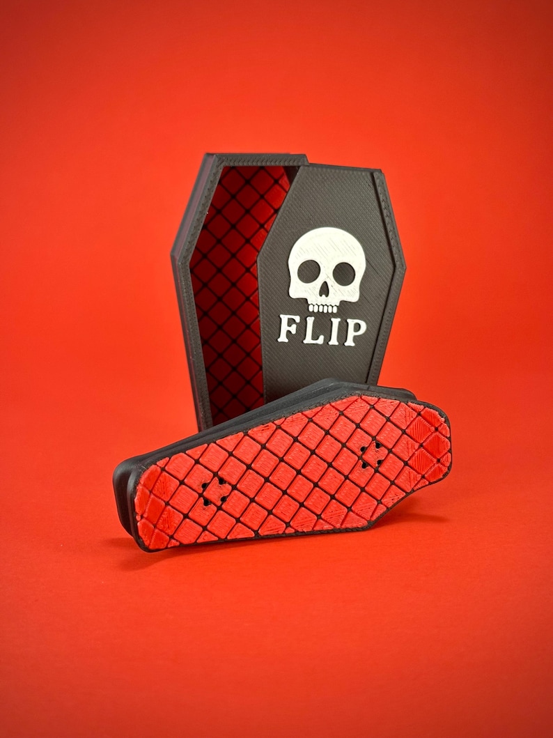 May include: A black coffin-shaped box with a red diamond pattern interior and a white skull graphic with the word "FLIP" on the front. A small black and red skateboard is in front of the box, on a red background.