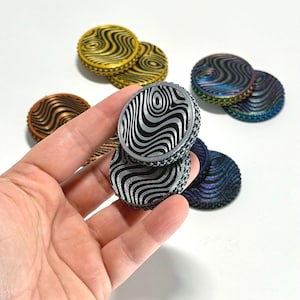 May include: Several decorative, circular objects with a distinctive wavy pattern design. The objects display a range of colours, including gold, copper, silver, and iridescent shades. The small, round objects appear to be made of metal.