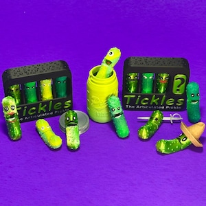 May include: A collection of articulated pickle toys with various facial expressions and accessories. Some pickles are in black boxes labeled "Tickles". One pickle wears a small sombrero. The background is a solid purple.
