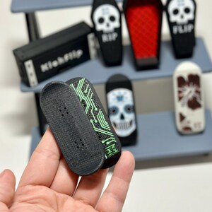 May include: A collection of miniature skateboards and coffin-shaped containers. The skateboards are black with green circuit board designs. The coffins are black with skull graphics and the word "RIP" or "FLIP".