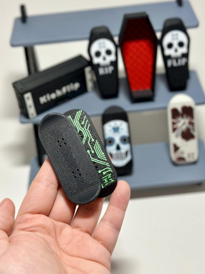 May include: A collection of miniature skateboards and coffin-shaped containers. The skateboards are black with green circuit board designs. The coffins are black with skull graphics and the word "RIP" or "FLIP".
