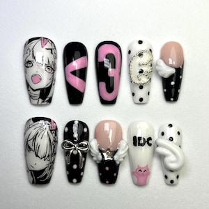 May include: A collection of ten artificial nails with diverse designs. The nails showcase black, white, and pink hues, incorporating polka dots, anime-style illustrations, and the number "3". Some nails have 3D embellishments such as wings and bows.