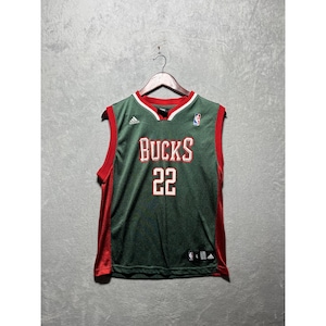 Può includere: Una maglia da basket senza maniche verde e rossa con la scritta "BUCKS" a blocchi bianchi e il numero "22". La maglia ha uno scollo a V e il logo NBA.