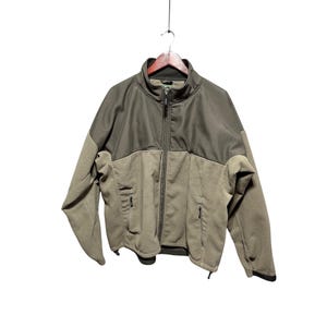 May include: A two-tone zip-up jacket in olive green and tan. The jacket has a high collar, two zippered pockets, and a full-length zipper. The jacket is hanging on a wooden hanger.
