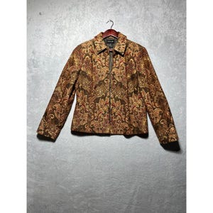 May include: A brown, gold, and red patterned jacket with a full-length zipper closure. The jacket has a collared neckline and long sleeves. The fabric features a detailed floral design. The jacket is hanging on a wooden hanger.