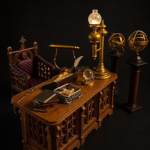 Op de afbeelding: Miniatuur houten bureau met sierlijke gravures, bekroond met boeken, een toverstaf en een zilveren dienblad. Een gouden lamp, twee globes en een stoel met een paars kussen maken de scène compleet. Het bureau is ongeveer 30 cm lang.