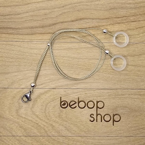 May include: A beige braided cord with a silver clasp and two clear plastic rings. The cord is looped and the rings are attached to the cord with silver beads. The text "bebob shop" is printed on a wooden surface.