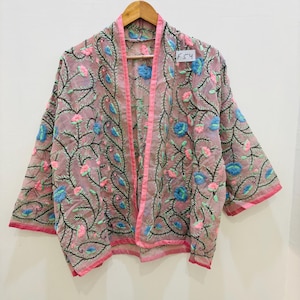 Könnte beinhalten: Eine transparente, hellrosa Jacke mit offenem Schnitt, verziert mit gestickten Blumenmustern in Blau, Rosa und Grün. Die Jacke hat einen rosa Besatz. Das Etikett lautet "F54".
