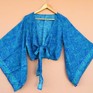 May include: A blue paisley-patterned wrap top with wide, flowing sleeves. The top is tied at the waist with matching fabric ties. The fabric has a detailed design in shades of blue and teal.