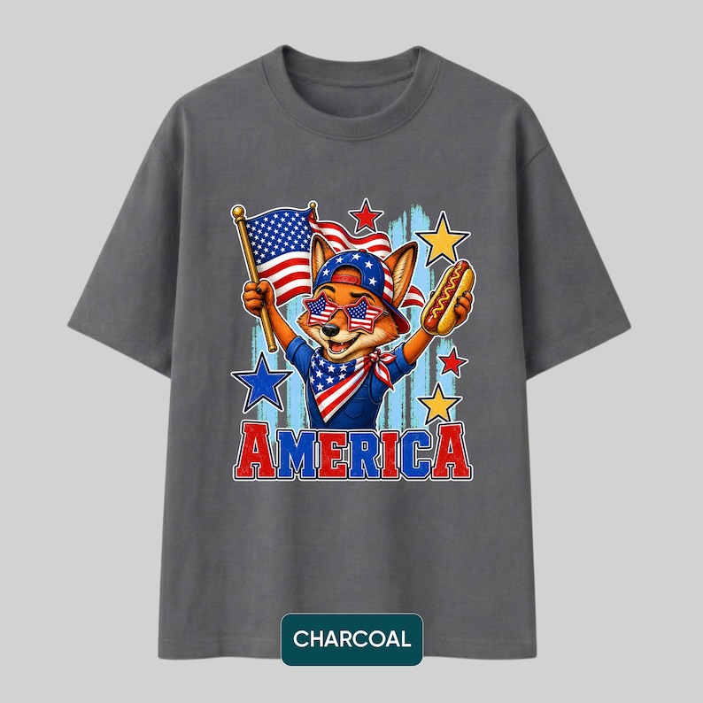 May include: A charcoal gray t-shirt featuring a graphic of a fox wearing star-spangled sunglasses, a bandana, and a cap. The fox holds an American flag and a hot dog. The word AMERICA is printed in red and blue below the illustration with stars.