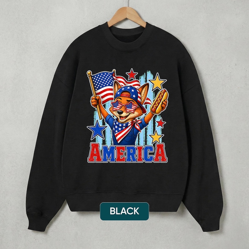 May include: A black crewneck sweatshirt featuring a graphic of a fox wearing a baseball cap and star-spangled sunglasses. The fox holds an American flag and a hot dog. The word AMERICA is printed in red and blue below the illustration with stars.