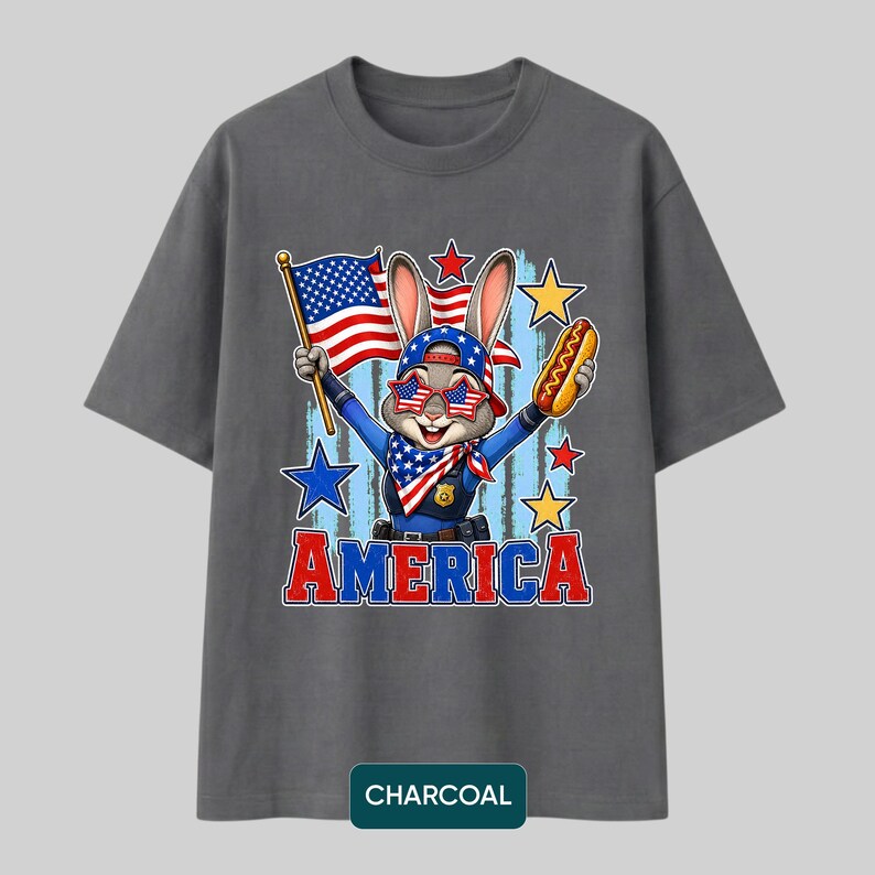 Puede incluir: Una camiseta gris carb&oacute;n con un gr&aacute;fico de un conejo vestido de polic&iacute;a, con gafas de sol estrelladas y una gorra. El conejo sostiene una bandera estadounidense y un perrito caliente. La palabra AMERICA est&aacute; impresa en rojo y azul debajo.