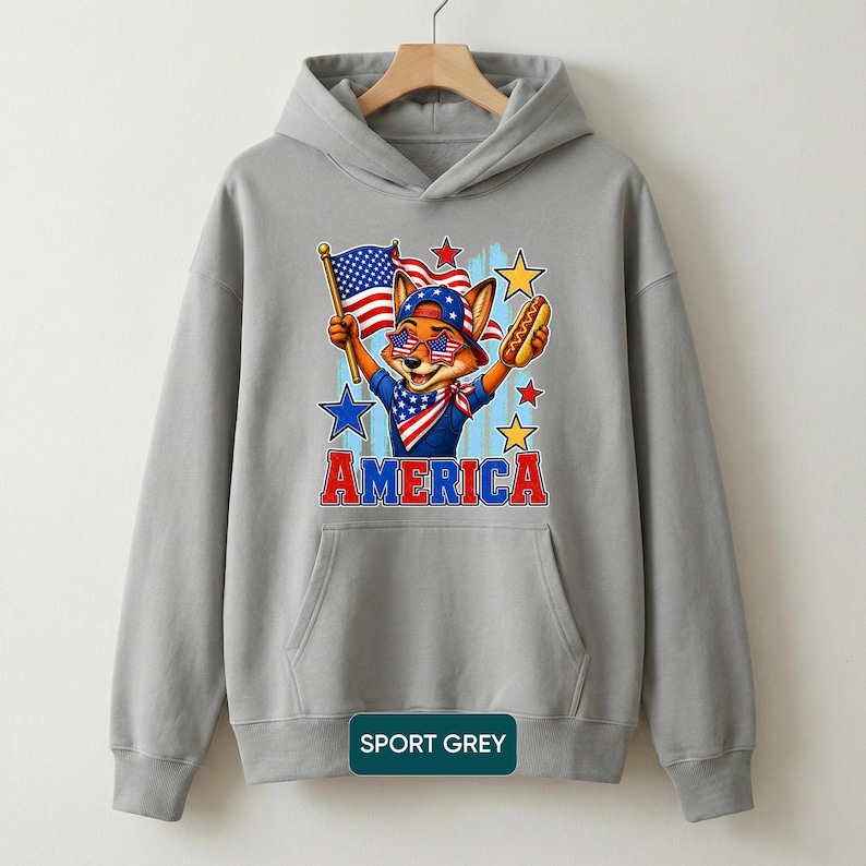 May include: A sport grey hooded sweatshirt featuring a graphic of a fox wearing star-spangled sunglasses and a bandana, holding an American flag and a hot dog. The word AMERICA is printed in red and blue block letters below the fox illustration.