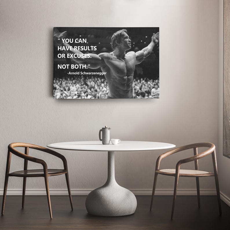 May include: Black and white canvas print featuring Arnold Schwarzenegger with the quote: "YOU CAN HAVE RESULTS OR EXCUSES. NOT BOTH." The print is displayed above a white table with two wooden chairs, creating a motivational and inspirational theme.