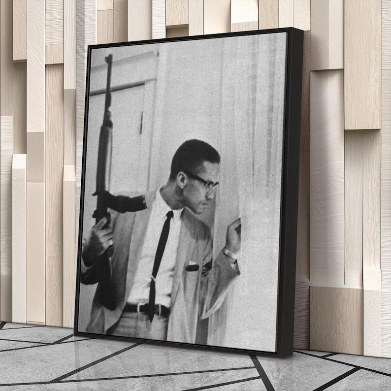 Op de afbeelding: Zwart-wit foto in een lijst van een man in een pak met een geweer. De man draagt een bril en een stropdas en kijkt naar rechts. De foto wordt getoond op een muur met een decoratief houten paneel.