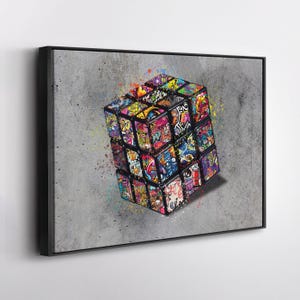 May include: A framed canvas print featuring a colorful Rubik's Cube with graffiti art. The cube is set against a gray background with paint splatters. The artwork showcases a vibrant mix of colors and designs.