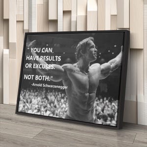 May include: Black and white framed canvas art featuring Arnold Schwarzenegger with the quote: "YOU CAN HAVE RESULTS OR EXCUSES. NOT BOTH." The image shows Schwarzenegger flexing in front of a crowd. The artwork is displayed on a wooden floor.