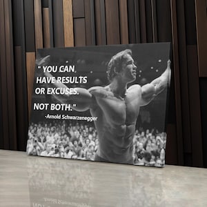 May include: Black and white motivational canvas print featuring Arnold Schwarzenegger with the quote: "YOU CAN HAVE RESULTS OR EXCUSES. NOT BOTH." The image shows Schwarzenegger flexing his muscles in front of a crowd.