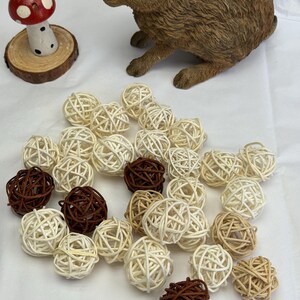 May include: A brown rabbit ornament and a red and white mushroom decoration are placed near a collection of woven rattan balls in shades of brown and cream. These decorative balls are ideal for home decor.