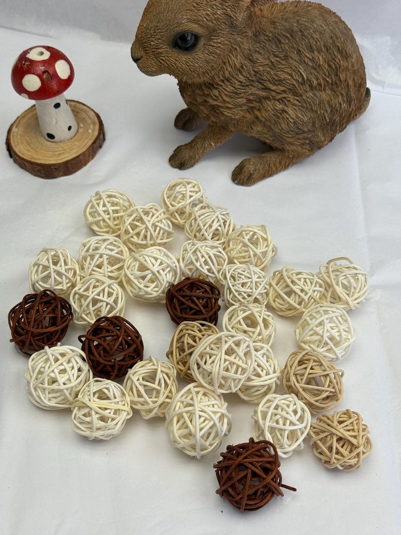 May include: A brown rabbit ornament and a red and white mushroom decoration are placed near a collection of woven rattan balls in shades of brown and cream. These decorative balls are ideal for home decor.
