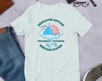 May include: Pale green t-shirt featuring a cartoon brain sleeping on a cloud, a blue mountain, and the text "Regulated Edition" and "Personally Victimized by my Nervous System".