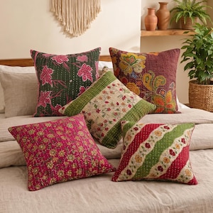 Könnte beinhalten: Fünf quadratische Zierkissen mit Kantha-Steppnähten und verschiedenen Mustern. Eines ist dunkelgrün mit rosa Blättern, eines kastanienbraun mit großen gelben Blumen, eines cremefarben mit Blumenranken, eines magentafarben mit kleinen Blumen und eines gestreift.