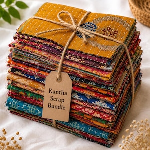May include: A stack of rectangular fabric pieces tied with twine and a brown paper tag labelled Kantha Scrap Bundle. The fabric features various colours including mustard yellow, deep red, blue, and green with intricate white running stitch patterns.