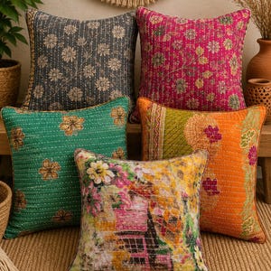 May include: Five square throw pillows featuring intricate kantha-style stitching. The collection includes a dark gray floral pillow, a vibrant magenta floral pillow, a green floral pillow, an orange patterned pillow, and a multicolored floral pillow.