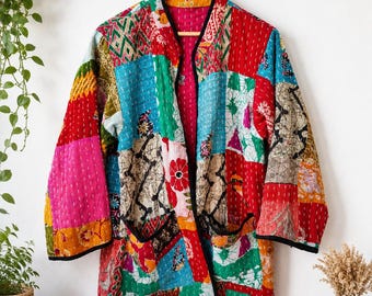 Puede incluir: Una chaqueta de manga larga con un diseño de patchwork hecho de varios cuadrados de tela coloridos en tonos rojo, azul, verde, amarillo y rosa. La prenda tiene un borde negro en los extremos, frente abierto y dos bolsillos delanteros.