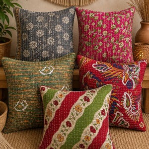 May include: A collection of five square throw cushions featuring kantha stitching. The cushions display various patterns including floral motifs, paisley designs, and diagonal stripes in colours of charcoal grey, magenta, olive green, and bright red.