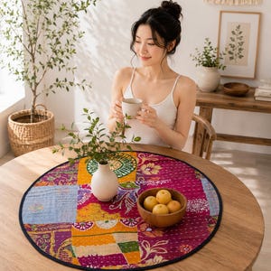 Peut inclure: Un tapis de table rond en patchwork multicolore présentant un mélange vibrant de carrés de tissu magenta, jaune et orange avec des motifs floraux et géométriques complexes, fini par une bordure bleu foncé et des points de couture blancs.