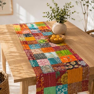 Könnte beinhalten: Ein rechteckiger Tischläufer mit einem Patchwork-Design aus verschiedenen Stoffquadraten in leuchtenden Farben wie Orange, Türkis, Gelb und Magenta. Der Läufer weist auf der gesamten Stoffoberfläche sichtbare weiße Steppnähte auf.
