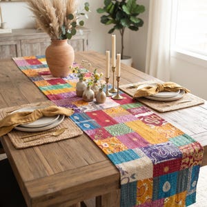 Könnte beinhalten: Ein rechteckiger Tischläufer mit einem lebendigen Patchwork-Design aus verschiedenen bunten Stoffquadraten mit komplizierten Mustern. Der Läufer liegt auf einem Holztisch, dekoriert mit einer Terrakotta-Vase, drei kleinen Vasen und Kerzen.
