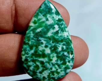 May include: A teardrop-shaped gemstone with a vibrant green and white mottled pattern. The polished surface reflects light, highlighting the natural variations in colour and texture. The stone is held in a hand, showcasing its size and shape.